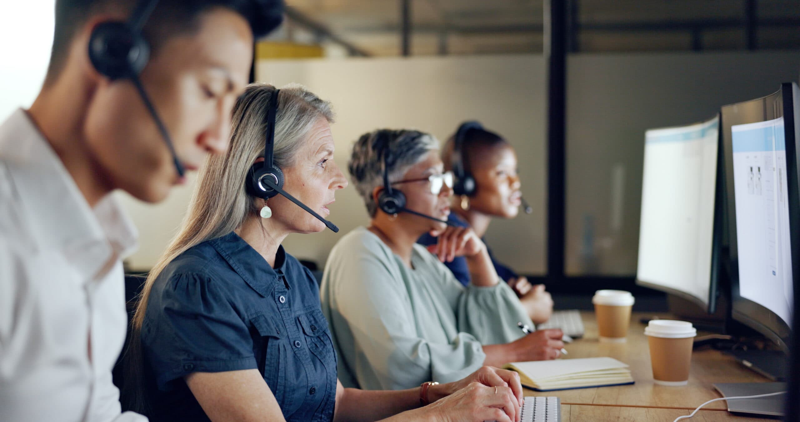 Senior call centre consultants with headphones, looking at computer, and talking to clients