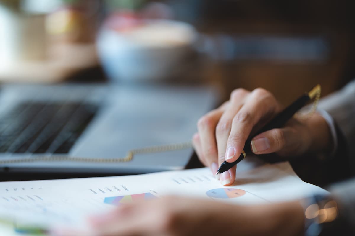 Woman reviewing a document and writing notes beside a laptop