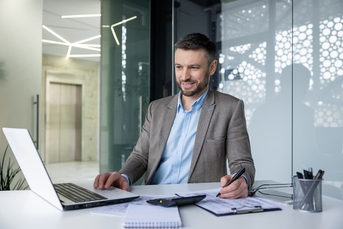 a smiling businessman at a desk looking at laptop