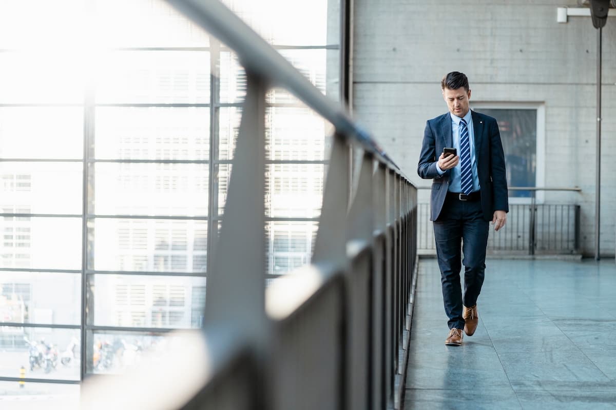 A business man checking his phone while walking outside a building