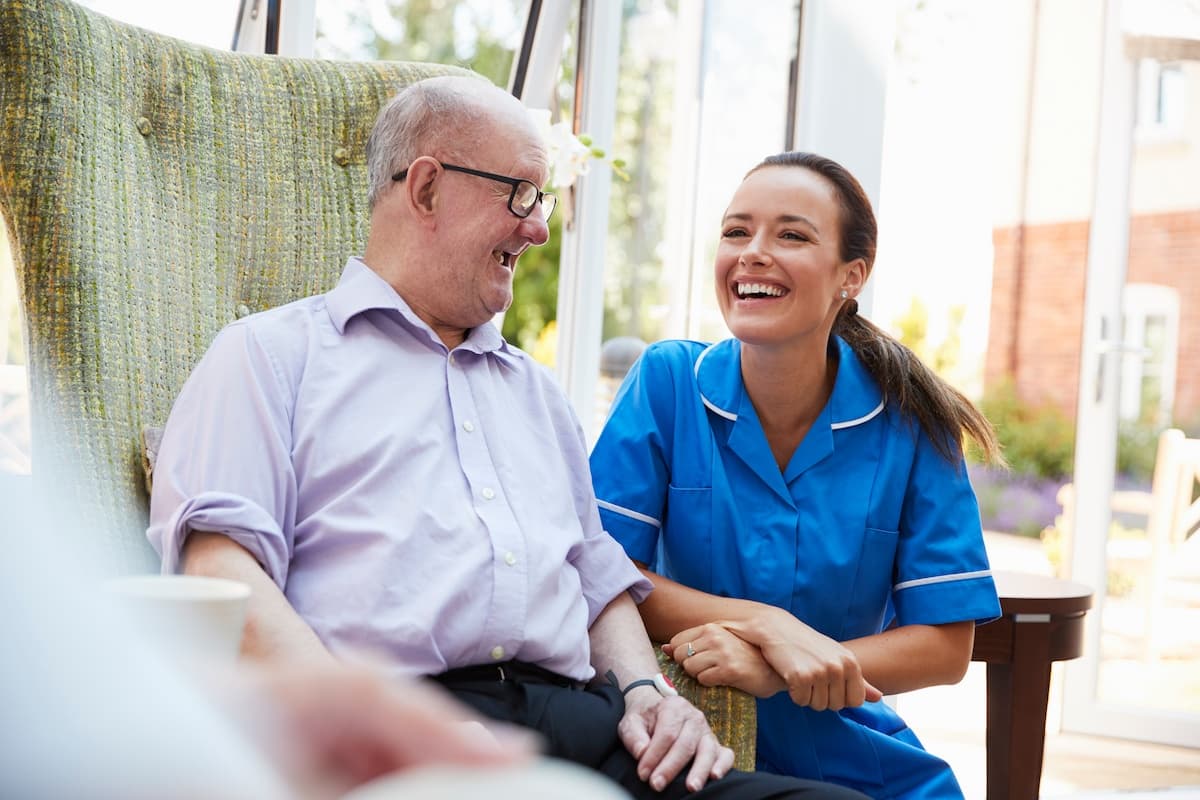 A smiling aged care female nurse with patient sitting down